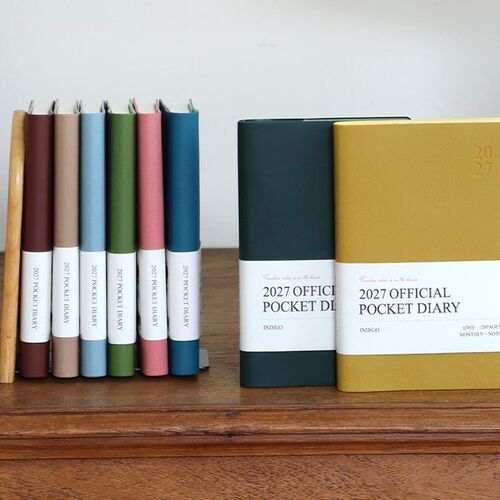 Several planners stand upright on a shelf, displaying their slim profiles and varied cover colors from the side.