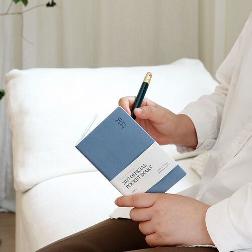 Water Blue is held open during a quiet writing moment, highlighting the planner’s portable pocket format.
