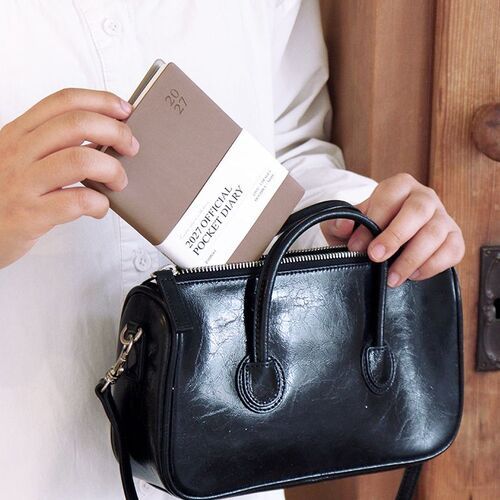 Mocha Mousse is being placed into a black handbag, demonstrating how the pocket planner travels with daily essentials.