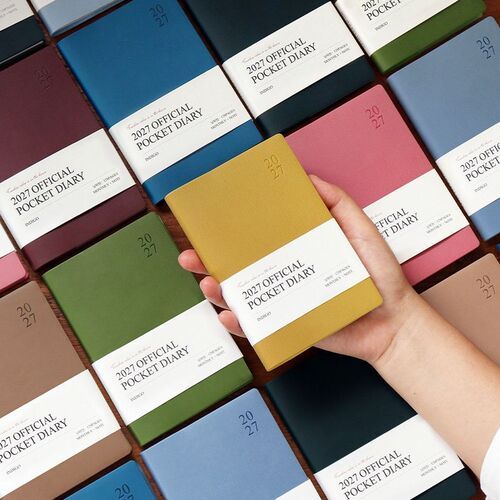 Multiple wrapped planners are spread across a wood surface, making the eight available cover colors easy to compare.