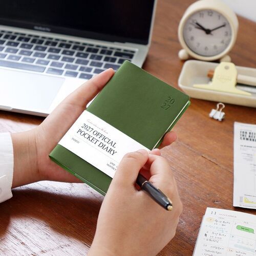 Mustard is held near a laptop and desk accessories, with its simple 2027 cover detail facing forward.