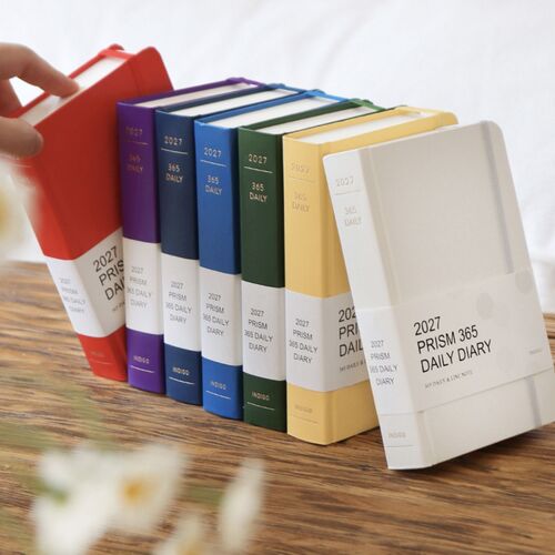 A row of colorful planners leans together on a wooden surface, highlighting their coordinated elastic bands and labeled 2027 spines.