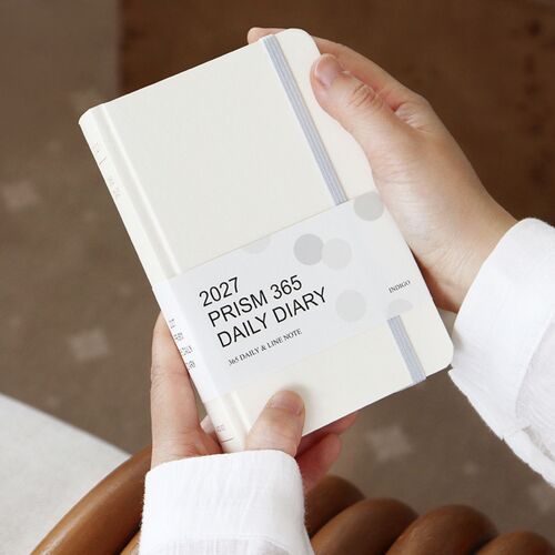 The Cloud planner is held in both hands with its paper belly band still attached and elastic closure visible.