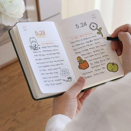 An open daily spread shows dated pages with spacious ruled writing areas and small illustrated accents near the headings.