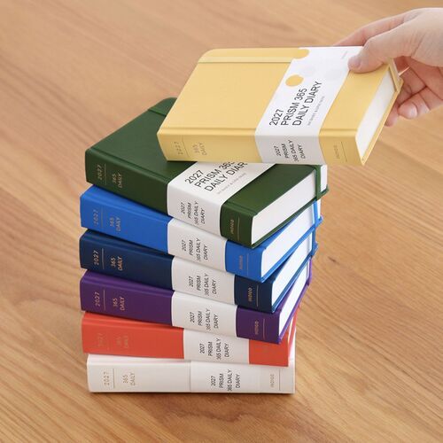 The Moss Green planner rests beside reading material, showing its textured cover, neat edges, and secure elastic band.