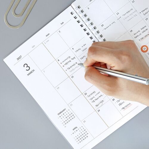 The open spread shows a monthly calendar filled with handwritten notes, stickers, and highlighted reminders.