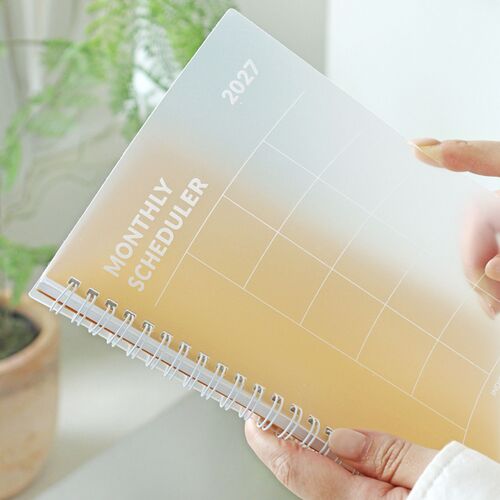 A Lavender planner is held against a bright background, with the cover grid and clear PP layer visible.