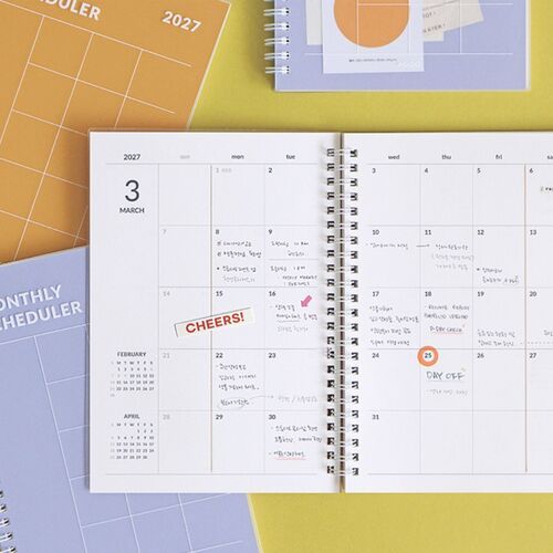 Lavender and Orange planners sit among open calendar pages and stationery, showing how the monthly layouts fit a planning setup.