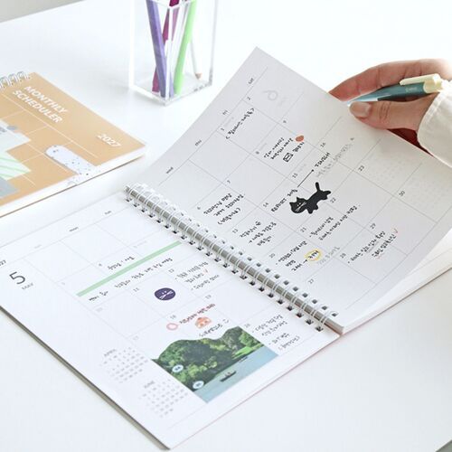 A March 2027 spread is being used with a pen, showing writing space across the dated calendar boxes.