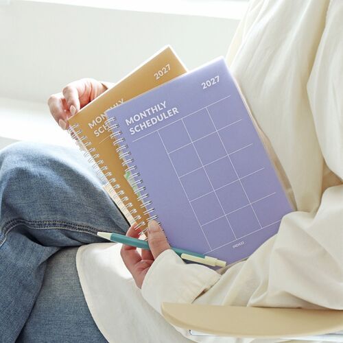 Lavender and Orange planners are displayed together in a relaxed setting, emphasizing their portable size and distinct cover colors.