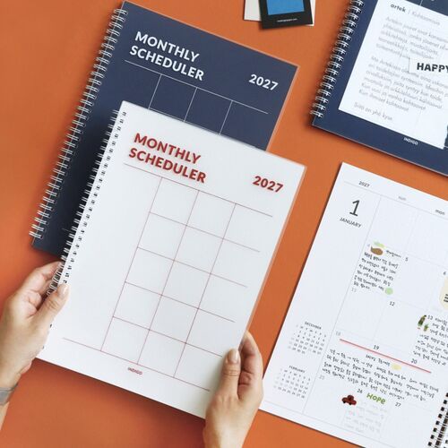 A hand-held view shows the planner opened wide, with the spiral binding centered between two usable pages.