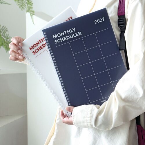The White planner is angled in hand, highlighting its large format, clear grid lines, and silver spiral binding.