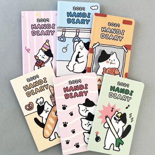 Six planners are arranged together to show the range of cat illustrations, from subway scenes and baguettes to music and birthday motifs.