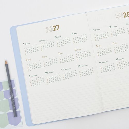 A hand opens the planner to a dated April 2027 spread with monthly calendars and lined sections.