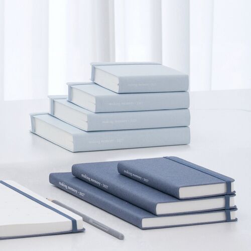 Three planners stand upright beside pencils, showing their compact proportions and elastic bands from the side.