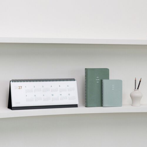 The calendar appears on a shelf beside coordinating planners, pencils, and a simple white vase.