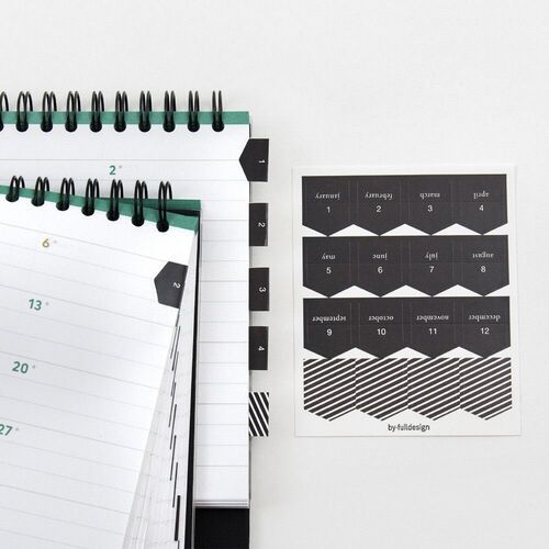 The side view highlights metric ruler marks along the translucent cover beside the stacked calendar pages.