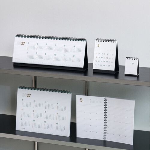 Several planners are arranged on shelving, showing the wide desk format alongside other calendar sizes for scale.