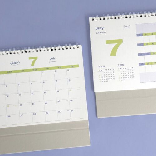 The calendar is photographed beside a book and pen, showing the upright display and crisp white pages with a green base.