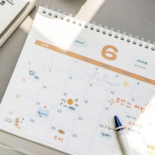 The cover is lifted to reveal an April calendar page, illustrating the spiral binding and double-sided page format.