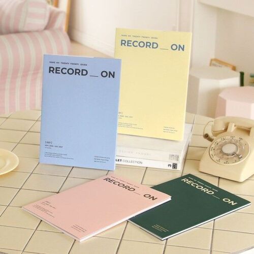 Four A4 planners are displayed together in Serenity Blue, Butter, Misty Pink, and Moss Green on a tiled tabletop.