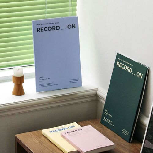 Serenity Blue and Moss Green planners are arranged near a bright window, showing their simple covers and large format.