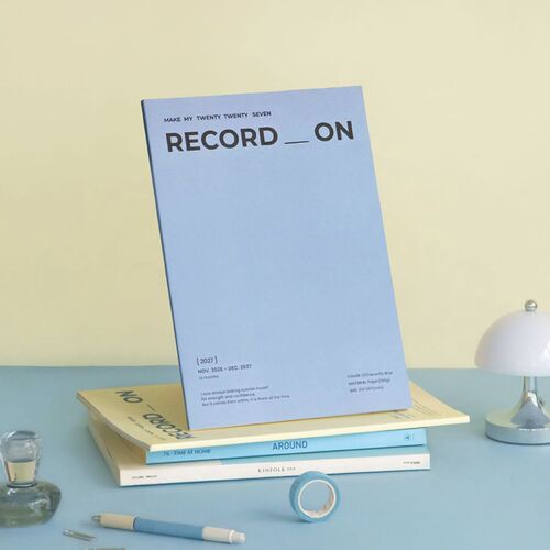 Several Record On planners rest on a wooden desk, with Butter and Misty Pink covers visible beside a pen.