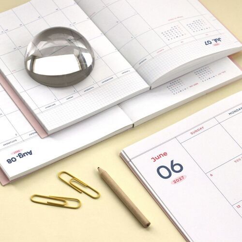 A Misty Pink planner sits beneath a transparent cover with postcards and printed images arranged across the front.
