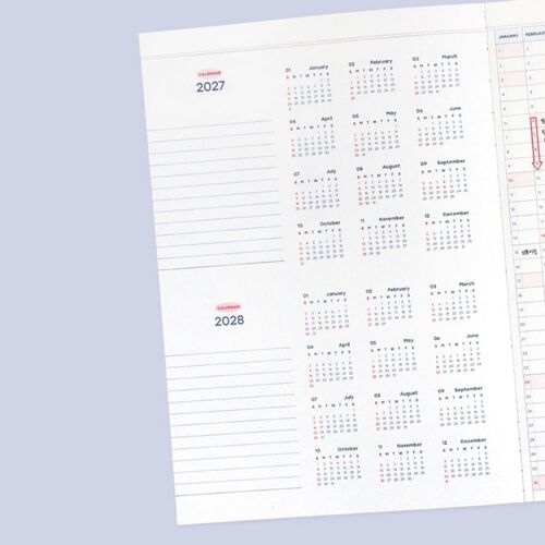 The planner is shown open across a pale surface, with repeated monthly calendars and spacious grid sections visible.