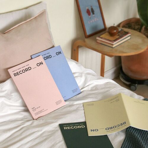 An open monthly planner is used at a desk, where a hand writes directly into the spacious calendar grid.