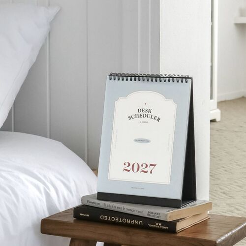 Placed on stacked books, the scheduler adds a calm planning spot beside a bed and reading area.