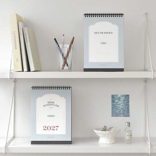An August page rests on stacked design books, with the black stand keeping the scheduler upright.