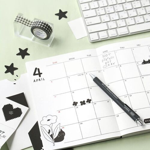 An open monthly spread shows the April calendar layout surrounded by decorative black-and-white desk accents.