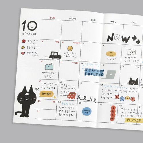 An open weekly spread shows large writing areas divided by weekday, with a black die placed above the page.