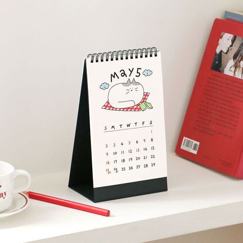 Photo 11: The May page shows a resting cat with blue flower accents and a compact monthly layout on a shelf.