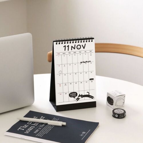 Photo 18: A hand holds the calendar open to a simple monthly page, highlighting the spiral binding and sturdy triangular base.