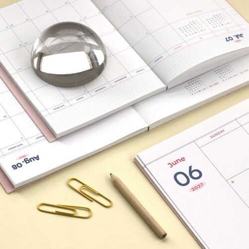 A close view of the pink planner shows its smooth cover and compact proportions beside desk supplies.
