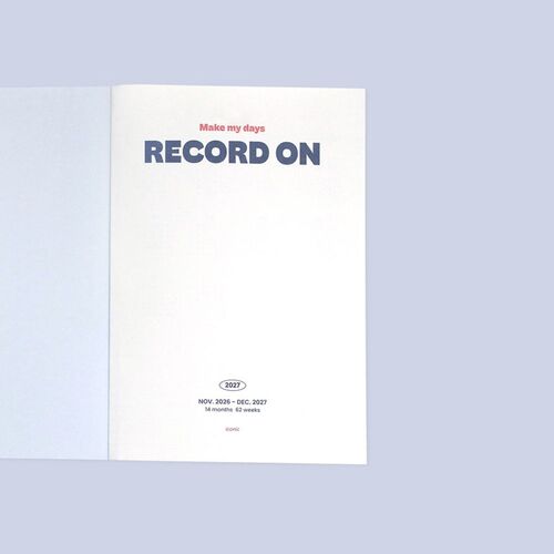 The planner opens flat to a monthly spread with spacious date boxes and navy-and-pink accents.
