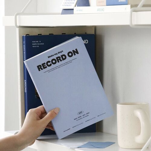 A shelf display shows the planner standing among books and desk objects in a tidy workspace.