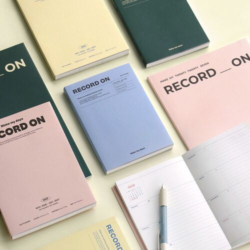 The four planners are fanned out in hand, making the Serenity Blue, Butter, Misty Pink, and Moss Green options easy to compare.