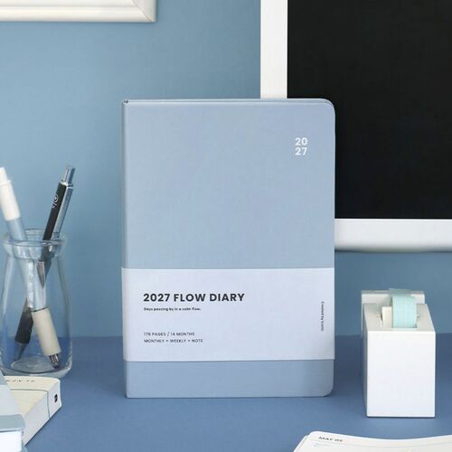 A planner lies open beside pens and desk tools, showing the monthly layout in a practical workspace setting.