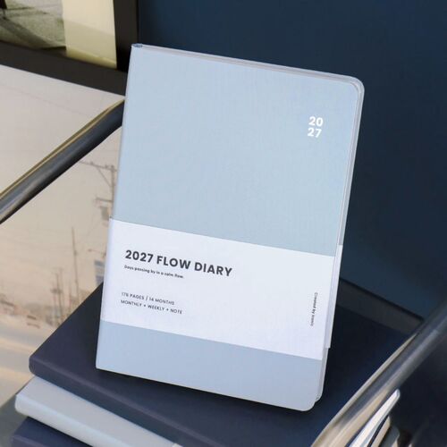 An open planner displays a monthly spread with a ribbon bookmark extending from the lower edge.