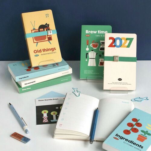 A tabletop arrangement shows an open planner, writing tools, and several cover styles together.