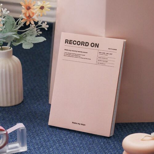 Misty Pink planner stands against a soft pink backdrop, showing its simple front design and visible page block.
