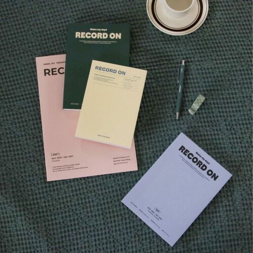 Serenity Blue, Butter, Misty Pink, and Moss Green planners are presented together beside a framed print and ceramic cup.