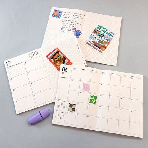 An open planner displays a lightly gridded writing page beside a decorated weekly layout with spacious areas for notes.