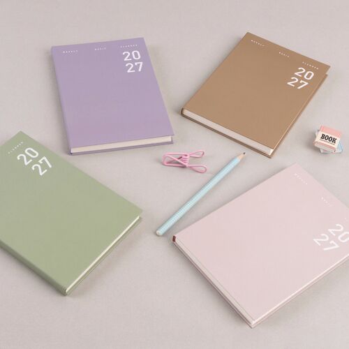 Sand Pink, Ash Purple, Sage Green, and Hazel planners are shown from above among simple desk accessories.