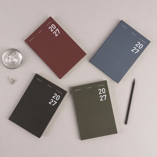 A dated July weekly spread is open beside glasses, stationery, and layered planner covers.