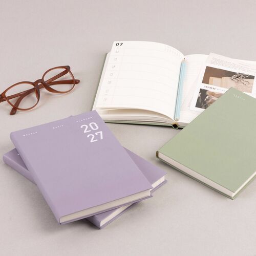 Burgundy and Navy Peony planners are opened beside their covers, showing dated pages and lined notes.